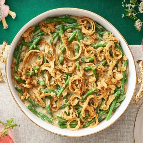 Overhead view of a festive holiday meal featuring a large serving dish of golden-brown Green Bean Casserole topped with crispy fried onions.