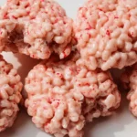 Close-up of pink, textured Marshmallow Rice Krispies Halloween Brains, speckled with red, on a white surface.