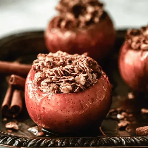 Warm baked apples, generously filled with cinnamon granola, glistening with syrup on an ornate dark tray.