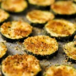 Close-up overhead view of golden-brown Baked Parmesan Zucchini slices on a baking sheet.