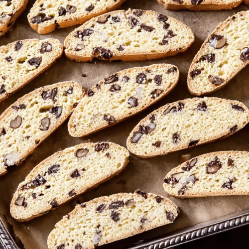 Close-up of golden-brown biscotti slices with chocolate and almonds on a baking sheet.