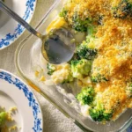 Overhead view of a freshly baked Broccoli Cheese Casserole with golden breadcrumbs, served alongside blue floral plates.