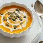 Rustic still life with a red pot of vibrant canned pumpkin soup, surrounded by garlic, star anise, and cinnamon sticks on a wooden board.