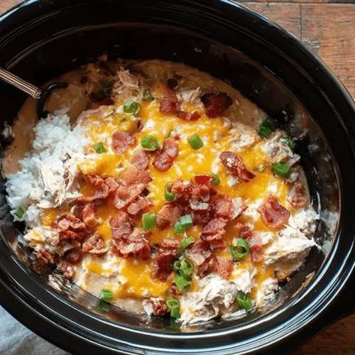 Overhead view of a creamy, cheesy crack chicken recipe with bacon and scallions served in a slow cooker.
