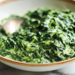 Appetizing close-up of classic Creamed Spinach served in an elegant white and gold-rimmed bowl with a silver spoon.
