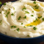 Close-up of a bowl of fluffy, parsley-garnished creamy mashed potatoes with melted butter.