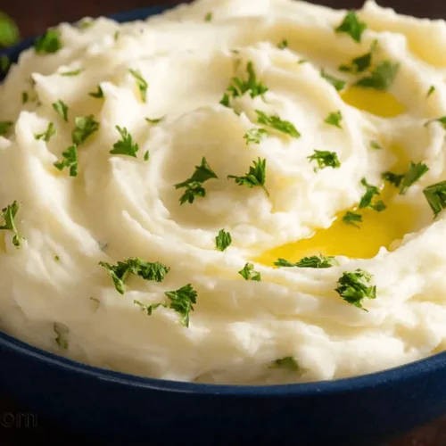 Close-up of a bowl of fluffy, parsley-garnished creamy mashed potatoes with melted butter.