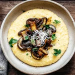 Overhead view of a hearty bowl of Creamy Polenta with Mushrooms, garnished with Parmesan and fresh parsley, on a rustic wooden table.