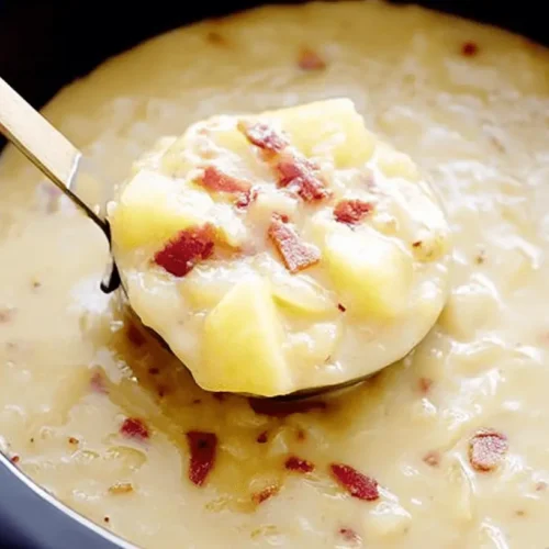 Overhead view of creamy crockpot potato soup with bacon bits, scooped from a dark pot.