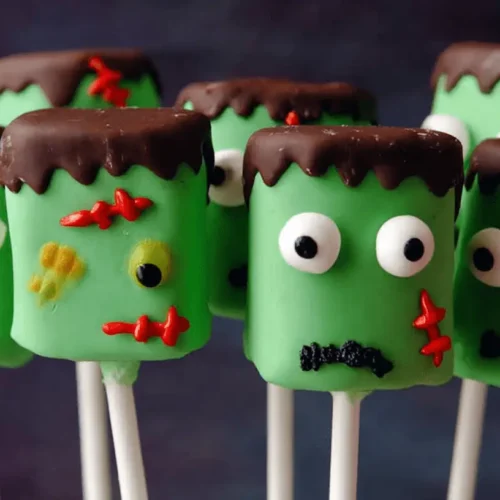 A charming cluster of vibrant green Frankenstein Marshmallow Pops with candy eyes, chocolate hair, and red stitches, ready for Halloween.