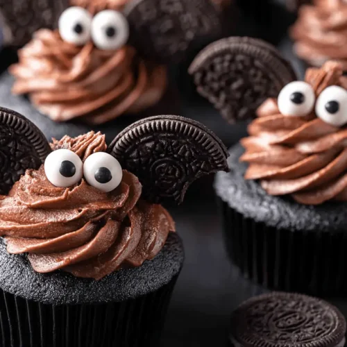 Delicious chocolate Halloween bat cupcakes with Oreo wings and candy eyes on a dark platter.