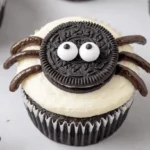 Close-up of charming chocolate halloween spider cupcakes with Oreo bodies and candy eyes on a light surface.