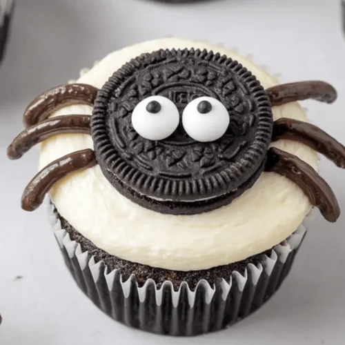 Close-up of charming chocolate halloween spider cupcakes with Oreo bodies and candy eyes on a light surface.