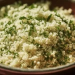 Close-up of a bowl of fluffy Herbed Couscous, generously mixed with fresh green parsley, served in a rustic terracotta bowl.
