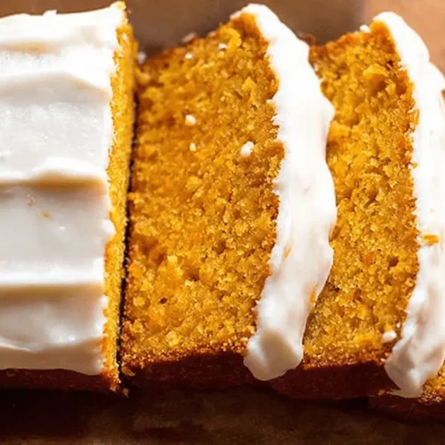 Delicious frosted keto pumpkin bread, sliced and ready to serve on parchment paper.