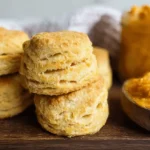Golden-brown pumpkin biscuits with flaky layers served on a rustic wooden board with orange spread.