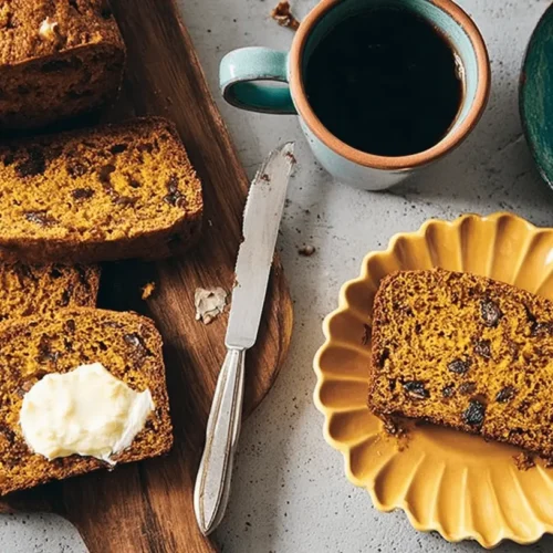 Freshly baked pumpkin bread loaf and slices on a wooden board with butter, a perfect representation of a delicious pumpkin bread recipe.