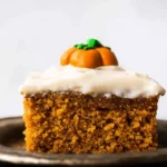 Delectable slice of pumpkin cake with creamy frosting and an edible pumpkin decoration.