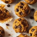 Delicious homemade pumpkin chocolate chip muffins with visible chocolate chips on a textured light surface.