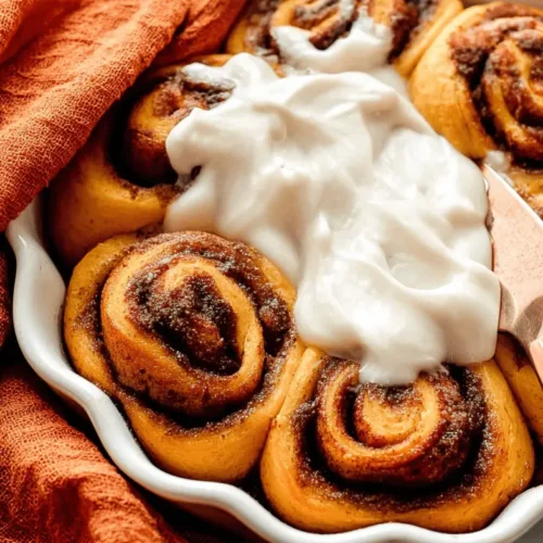 Overhead view of a baking dish filled with golden-brown pumpkin cinnamon rolls, generously frosted and ready to serve in an autumnal setting.