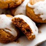 Close-up of freshly baked, soft pumpkin cookies with white glaze and spice on a rustic plate.
