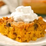 A delicious slice of vibrant orange pumpkin dump cake topped with fluffy whipped cream on an ornate, off-white plate.