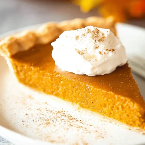 A delectable slice of pumpkin pie topped with whipped cream and spices, presented on a light plate with a warm, autumnal setting.