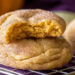 Freshly baked pumpkin snickerdoodle cookies, one with a bite taken out, showing its moist, golden interior and cinnamon sugar coating.