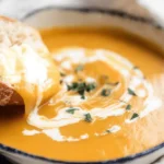Hand dipping rustic bread into a creamy, vibrant pumpkin soup.