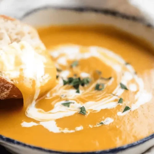 Hand dipping rustic bread into a creamy, vibrant pumpkin soup.