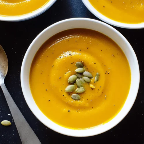 Overhead view of creamy golden pumpkin soup garnished with pumpkin seeds and black pepper, illustrating a delicious pumpkin soup recipe.