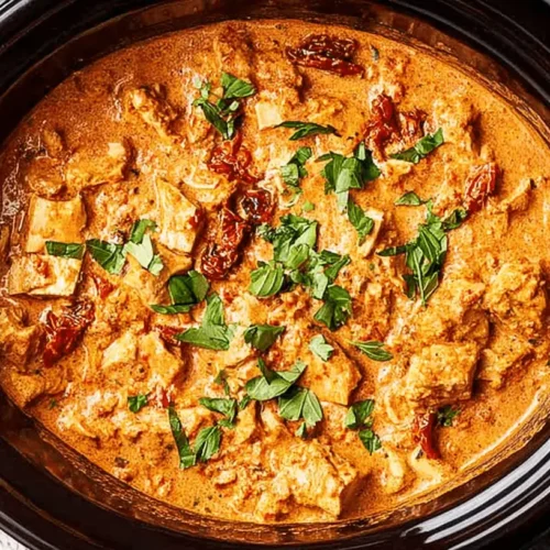 Overhead view of a delicious Slow Cooker Marry Me Chicken, rich with chicken and sun-dried tomatoes, garnished with fresh basil in a dark ceramic pot.