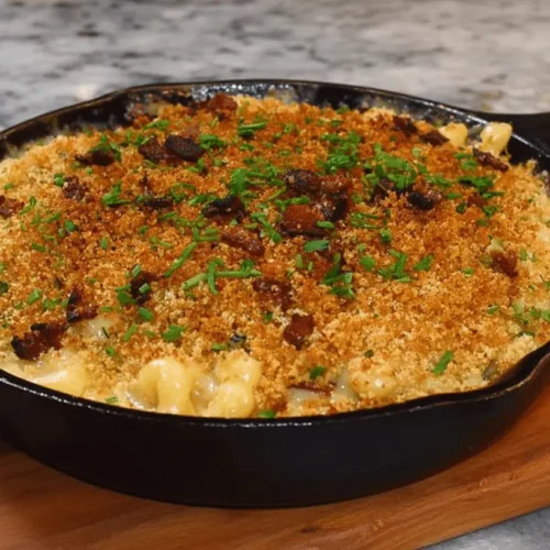 Hearty Thanksgiving Mac and Cheese baked in a cast-iron skillet with a crispy breadcrumb and bacon topping, garnished with fresh herbs.