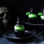 Dark Halloween still life with vibrant green witch cupcakes, chocolate hats, and an eerie skull.