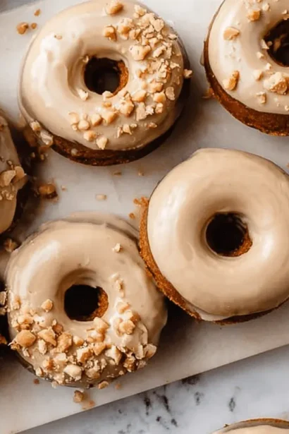 Overhead view of glazed and nut-topped Baked Pumpkin Donuts arranged on white marble.