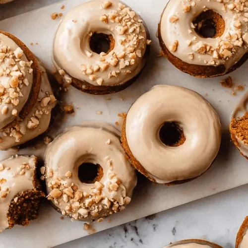 Overhead view of glazed and nut-topped Baked Pumpkin Donuts arranged on white marble.