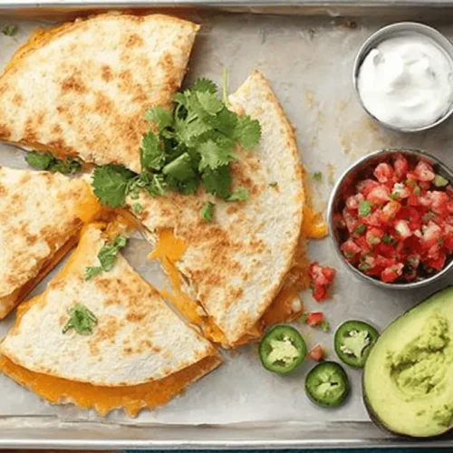Delicious golden-brown Baked Quesadillas cut into wedges, served with sour cream, salsa, avocado, and jalapeños on a metal baking sheet.