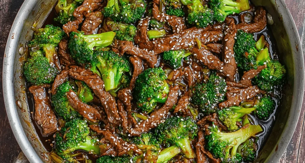 High-angle view of a delicious beef and broccoli stir-fry in a metal pan, garnished with sesame seeds.