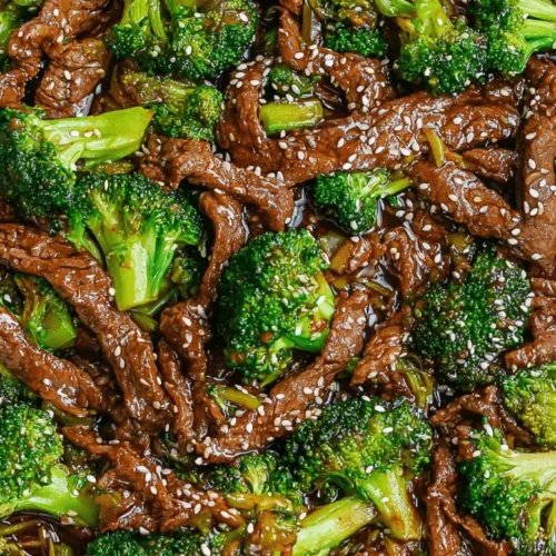 High-angle view of a delicious beef and broccoli stir-fry in a metal pan, garnished with sesame seeds.