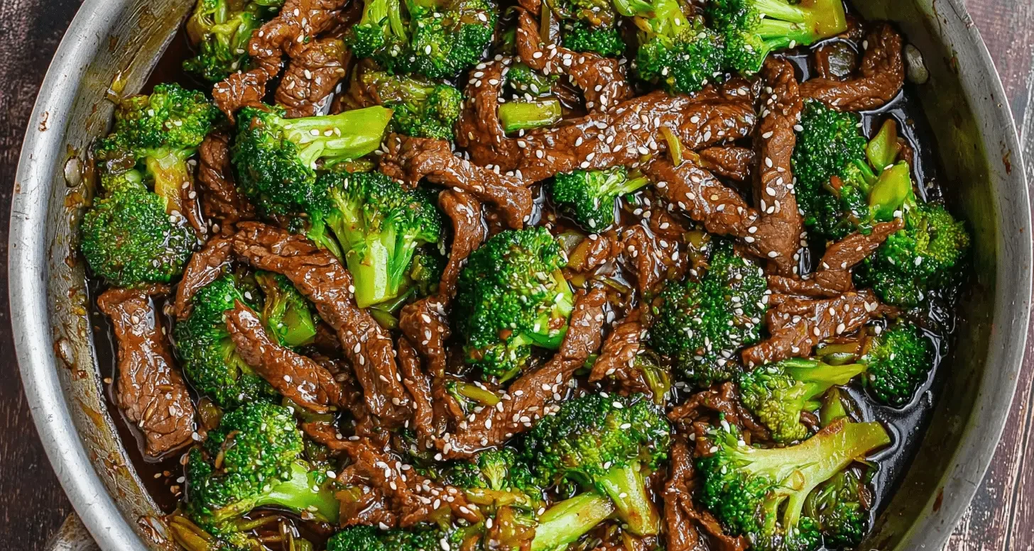 High-angle view of a delicious beef and broccoli stir-fry in a metal pan, garnished with sesame seeds.
