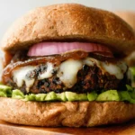 Appetizing close-up of a gourmet Black Bean Burger with avocado, melted cheese, and caramelized onions on a wooden board.