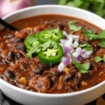 Close-up of a delicious bowl of Black Bean Chili garnished with jalapeños, red onion, and cilantro, ready to be enjoyed.