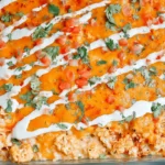 Vibrant and appetizing Buffalo Chicken Cauliflower Casserole, freshly baked with melted cheese, white drizzle, and green herbs in a glass dish.
