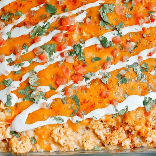 Vibrant and appetizing Buffalo Chicken Cauliflower Casserole, freshly baked with melted cheese, white drizzle, and green herbs in a glass dish.