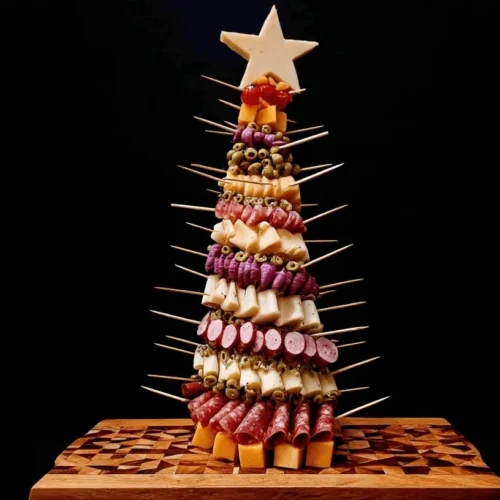 A vibrant Charcuterie Tree made with cheese, cured meats, and olives on a decorative wooden board against a black background.