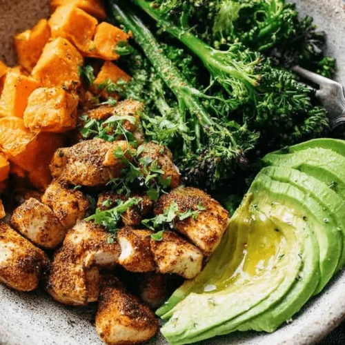 Overhead view of a vibrant Chicken and Sweet Potato Meal Prep bowl with broccolini and avocado.
