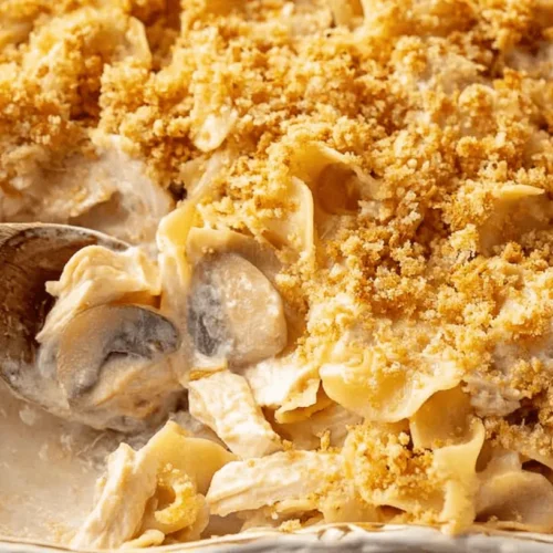 Creamy chicken and mushroom noodle casserole with a golden breadcrumb topping, being scooped from a white dish, inspiring delicious chicken casserole recipes.