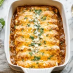 Golden-brown baked Chicken Enchiladas garnished with fresh cilantro and crumbled cheese, ready to serve on a white marble surface.