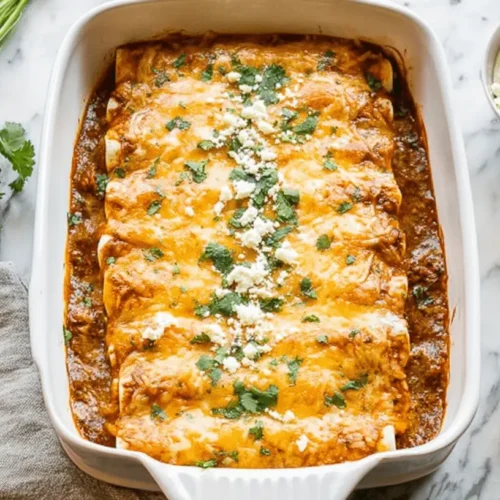 Golden-brown baked Chicken Enchiladas garnished with fresh cilantro and crumbled cheese, ready to serve on a white marble surface.