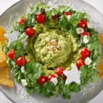 A festive Christmas Wreath Guacamole dip, garnished with cherry tomatoes, cilantro, and white cheese, surrounded by star, Christmas tree, and reindeer-shaped tortilla chips on a light grey plate.